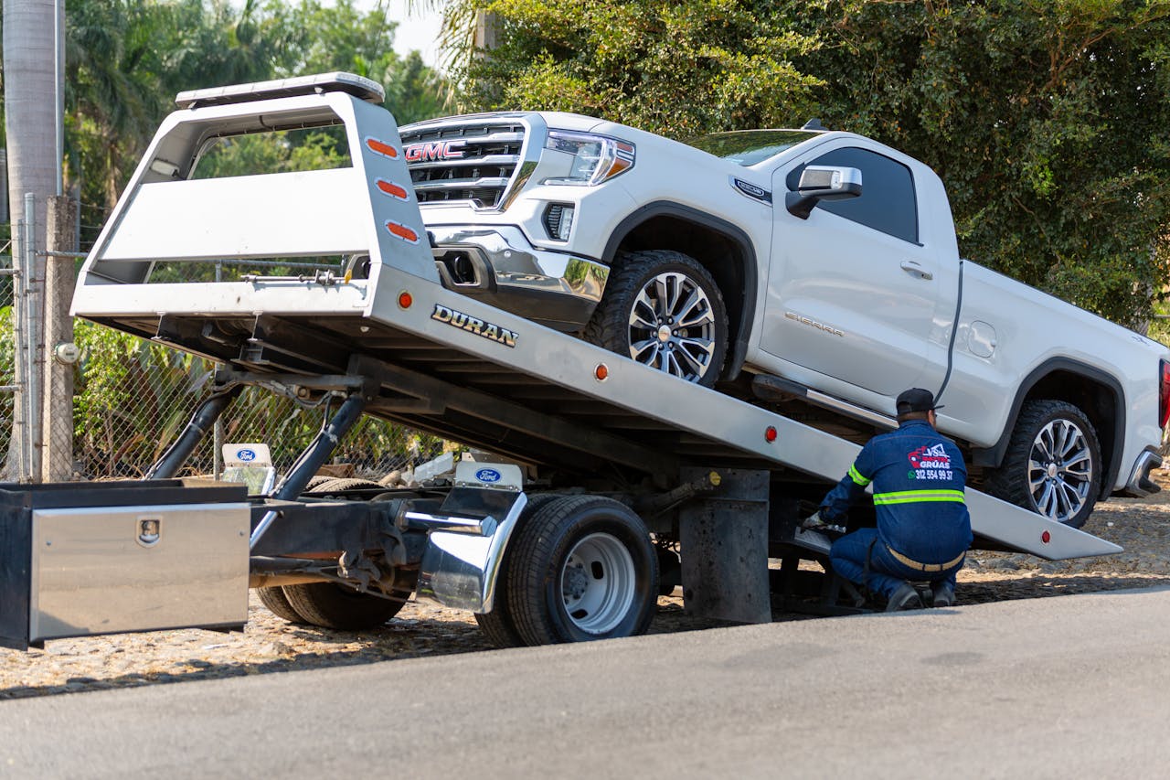 brand-02 Tow truck operator loading white GMC pickup truck on street in daytime.