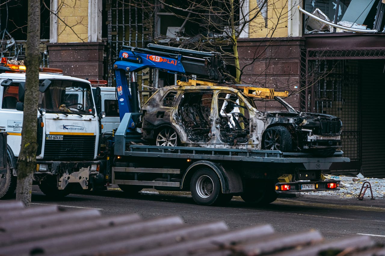 digital A burnt car is towed on a street in Kyiv, highlighting the aftermath of conflict.