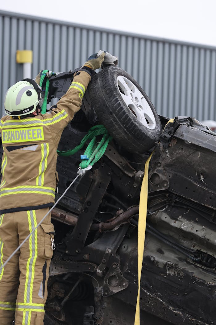 Services-03 Firefighter in protective gear secures overturned car at an accident scene with ropes and equipment.