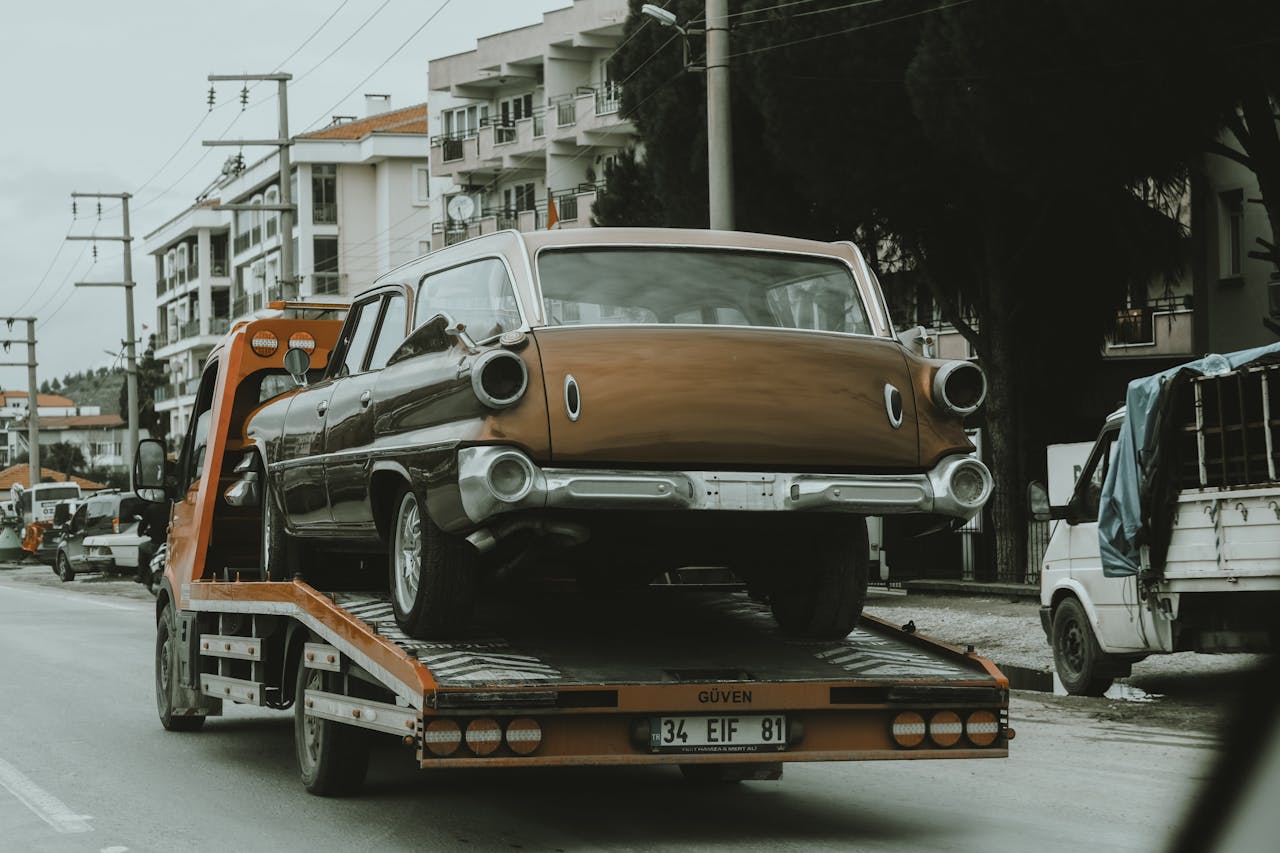 creative-03 A vintage car loaded on a tow truck in a city street, surrounded by modern buildings.